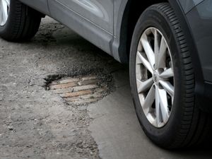 A silver car drives near to a pothole