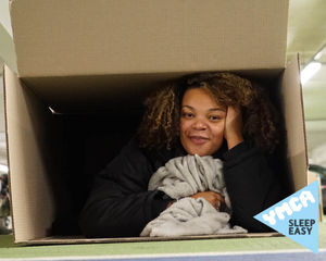 Young woman lying in a cardboard box to raise money to support young people moving on from homelessness