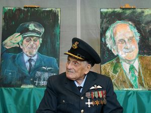 The last known Battle of Britain pilot, Group Captain John ‘Paddy’ Hemingway, in his military uniform, sits in front of a series of portraits