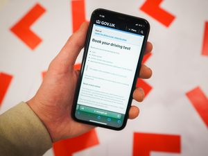 A driving test page on the gov.uk website shown on a phone next to driving L plates