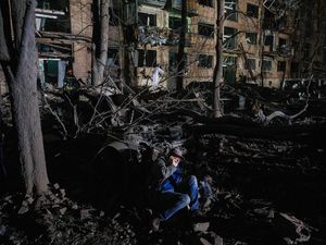 A man sits on the ground outside a house damaged by a Russian air strike in a residential neighborhood in Kyiv
