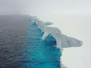 A drone view of the white top and pitted edge of Iceberg A23a in the Southern Ocean, with pale blue water below and darker water further away