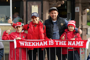 Wrexham fans pose behind a boundary during a victory parade in Wrexham