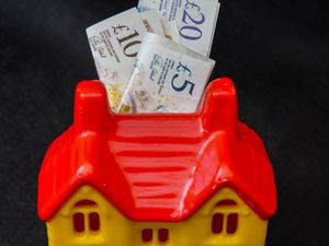A house-shaped money box with bank notes pushed into it