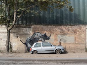 Supporting image for story: Banksy unveils rhino art that looks as though animal is climbing on a car