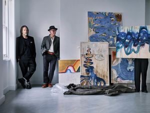 Two men standing near a series of blue paintings