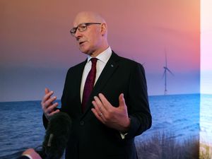 John Swinney gesturing with his hands as he speaks to the media