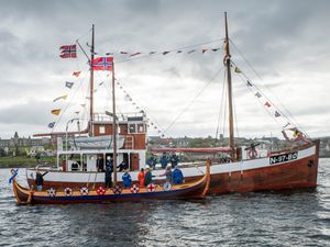 A fishing vessel alongside a boat decorated with shields