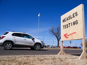 A vehicle drives past a sign outside of Seminole Hospital District offering measles testing in Seminole, Texas