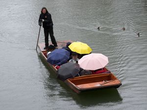 People shelter from the rain under umbrellas as they punt along the River Cam in Cambridge