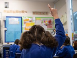 The back of a schoolgirl in blue jumper in class, with her hand up