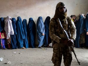 A Taliban fighter stands guard as women wait to receive food rations distributed by a humanitarian aid group in Kabul, Afghanistan