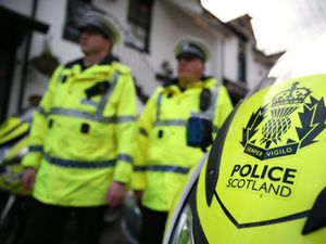 Police Scotland officers in uniform, walking past a police motorbike
