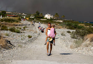 A man carries a child as they leave an area where a forest fire burns, on the Greek island of Rhodes. Photo: Lefteris Diamanidis/InTime News via AP.