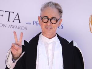 Alan Cumming on the Bafta TV red carpet event holding a peace sign with his two fingers
