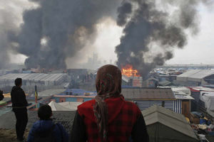 People stand on a hill as smoke and flames rise from amidst the tents yesterday