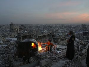 A boy and his mother cook on a fire on the roof of their house in Gaza surrounded by destroyed buildings