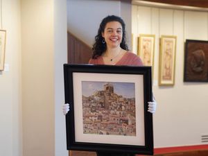 A smiling woman holds up the watercolour Bouleternere, which is mounted in a black frame