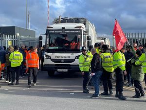 A white wagon leaving a waste depot with striking workers and police officers