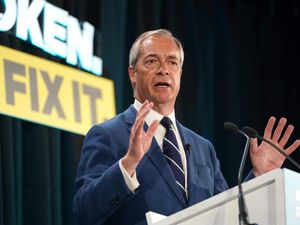 Nigel Farage gesturing with both hands while speaking from a lectern