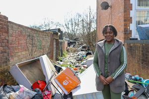 Image shows resident Patricia Burton standing next to fly-tipping pile at the rear of Slade Road in Stockland Green, Birmingham. 