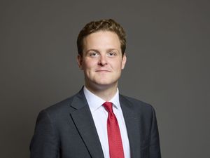 Official portrait of Oliver Ryan in a black suit and red tie