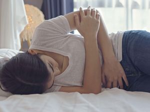 Woman lying on bed, suffering from stomach pain