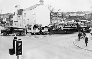 A long load negotiating the Cock Hotel crossroads in Wellington on January 11, 1975. The caption reads: 'A real traffic-stopper! This 96-ton load was given a police escort through Telford at the weekend to a Brierley Hill steelworks. The load - part of a crane - left the Adamson Alliance works at Horsehay on Saturday morning and arrived at its destination without incident. It is seen here on the A5 at Wellington.' The hauling vehicle was from Wrekin Roadways. The bicycle shop on the corner is H Sutch, selling Raleigh bikes