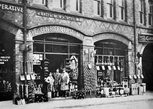 The premises in Market Drayton of 'The John Rodenhurst Limited.' It looks like an ironmongers. Written above is 'T.D. Hockenhull.' Glimpsed far right is a garage and there is also an RAC sign. The people standing outside will be the staff/shopkeeper. The back of this print is completely blank. Possibly taken around 1914? Glimpsed on the left is what we know from another picture is Silverdale Cooperative Society. If we were able to look further up on the facade of this building we would see the wording Raven Foundry and General Implement Warehouse. 