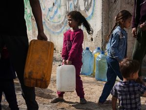 A young girl holds a large container of water in a refugee camp