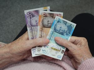 The hands of an elderly woman holding a £20, £10 and £5 note