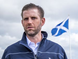 Head and shoulders photo of Eric Trump, with a Scottish flag in the background