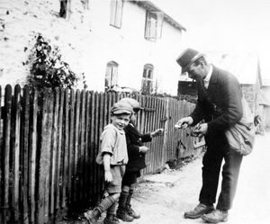Postman Charlie Williams with some young boys in Churchstoke. Dick Williams says he was given the photograph of his father by Malcolm Jones, it was taken by his mother in 1932. It is believed he is handing over stamps to a young boy who was holding out some money for them. The boy on the left is Mr Jones, and the other lad was Os Francis. The location is Cwm Cae, Pentre, Churchstoke. 