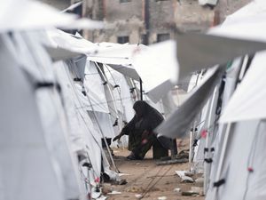 A displaced Palestinian woman cooks in a sprawling tent camp adjacent to destroyed homes and buildings in Gaza City