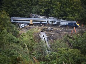 Aerial view of a derailed train, including one carriage that has come to rest down an embankment