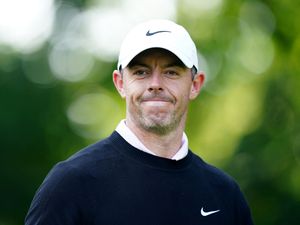 Rory McIlroy on a golf course wearing a white cap and dark jumper