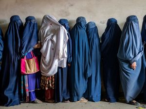 Afghan women wait to receive food rations distributed by a humanitarian aid group