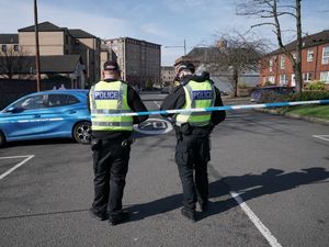 Two police officers standing beside police tape, which cordons off a road