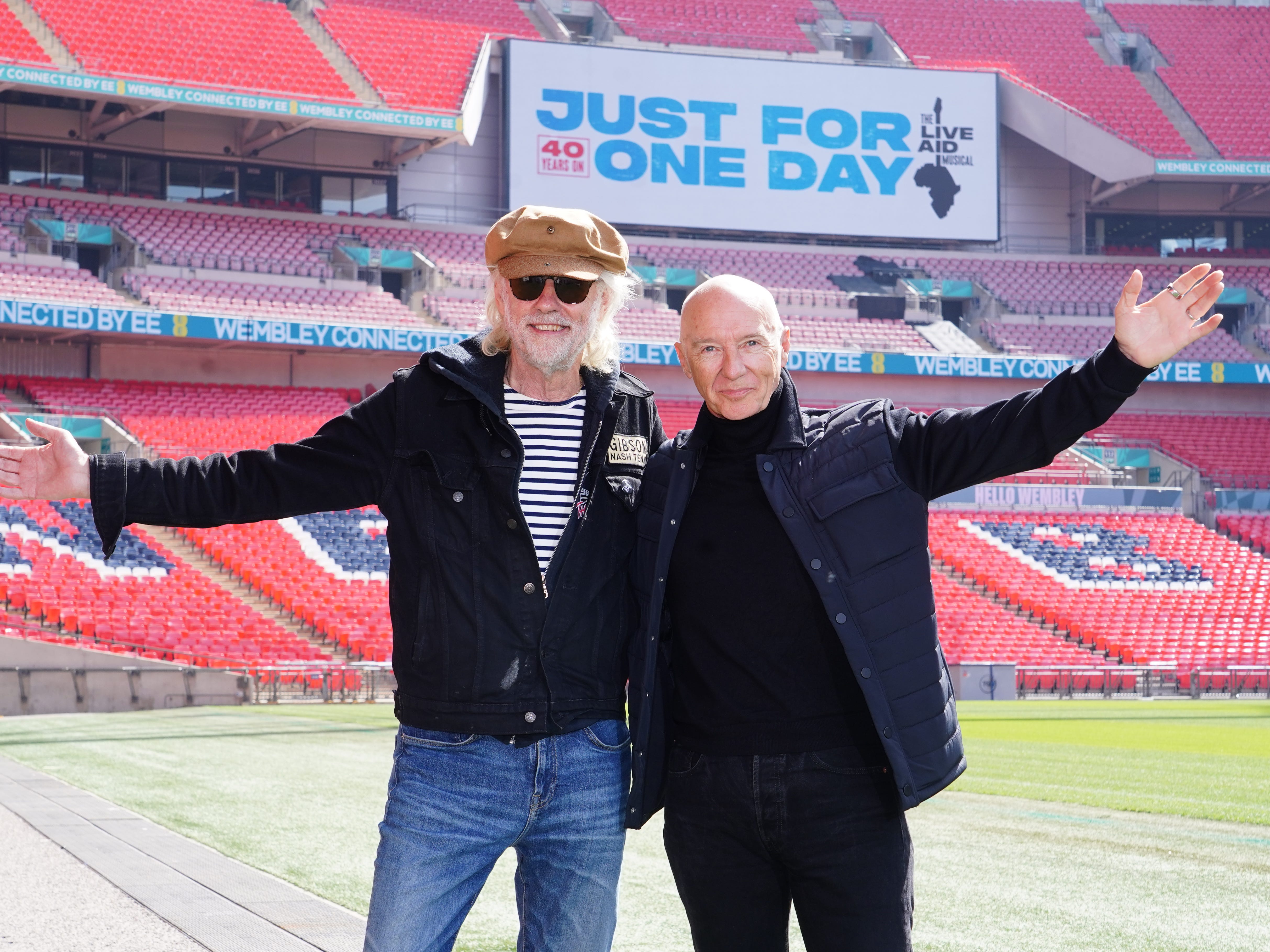 Bob Geldof and Midge Ure on the pitch at Wembley with a Just For One Day promotional sign behind