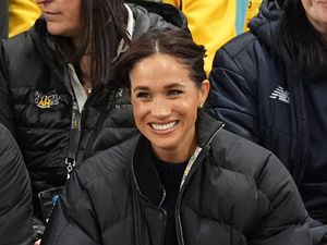 Meghan grins as she sit and watches the Invictus Games while wearing puffa jacket