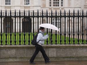 A woman shelters from the rain under an umbrella as she passes Senate House in Cambridge