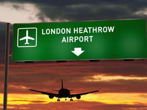 Plane silhouette landing at Heathrow, with airport direction signboard and sunset in background