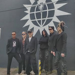 Pop Will Eat Itself pose in front of the artwork which bears their name