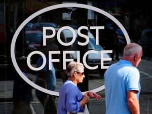 People walk past a window with a Post Office sign