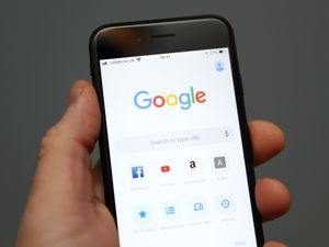 Hand holding a mobile phone showing Google search engine