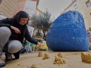 A woman places sand moulds next to a funnel-shaped sculpture that, as it turns on itself, draws on the ground a map of the towns affected by floods