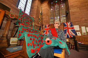 Looking at a cascade of poppies decorating a window, St Nicholas Knitters and Crafters member Elaine Burborough, at St Nicholas Church, Newport