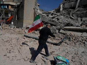 A man carries an Iranian flag to place on the rubble of a police facility struck during the US–Israeli military campaign in Tehran, Iran