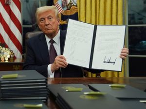 President Donald Trump holds up an executive order commuting sentences for people convicted of January 6 offences in the Oval Office of the White House