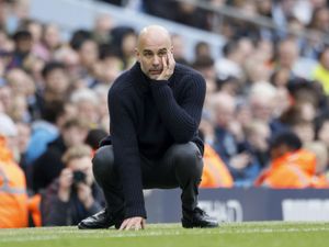 Pep Guardiola crouches down in apparent frustration on the touchline during a game